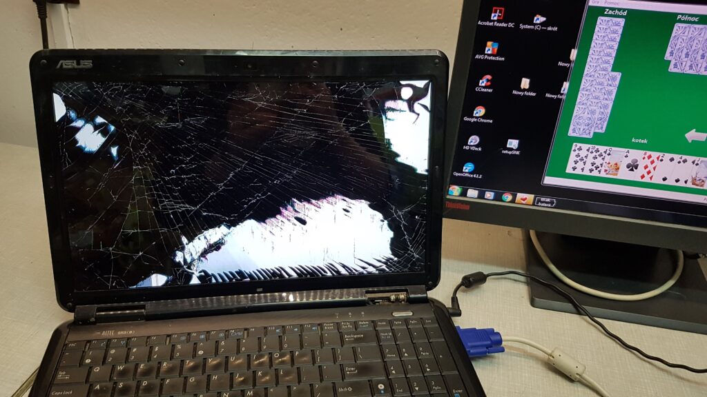 Laptop ASUS z rozbitą matrycą na stanowisku serwisowym, obok monitora komputerowego