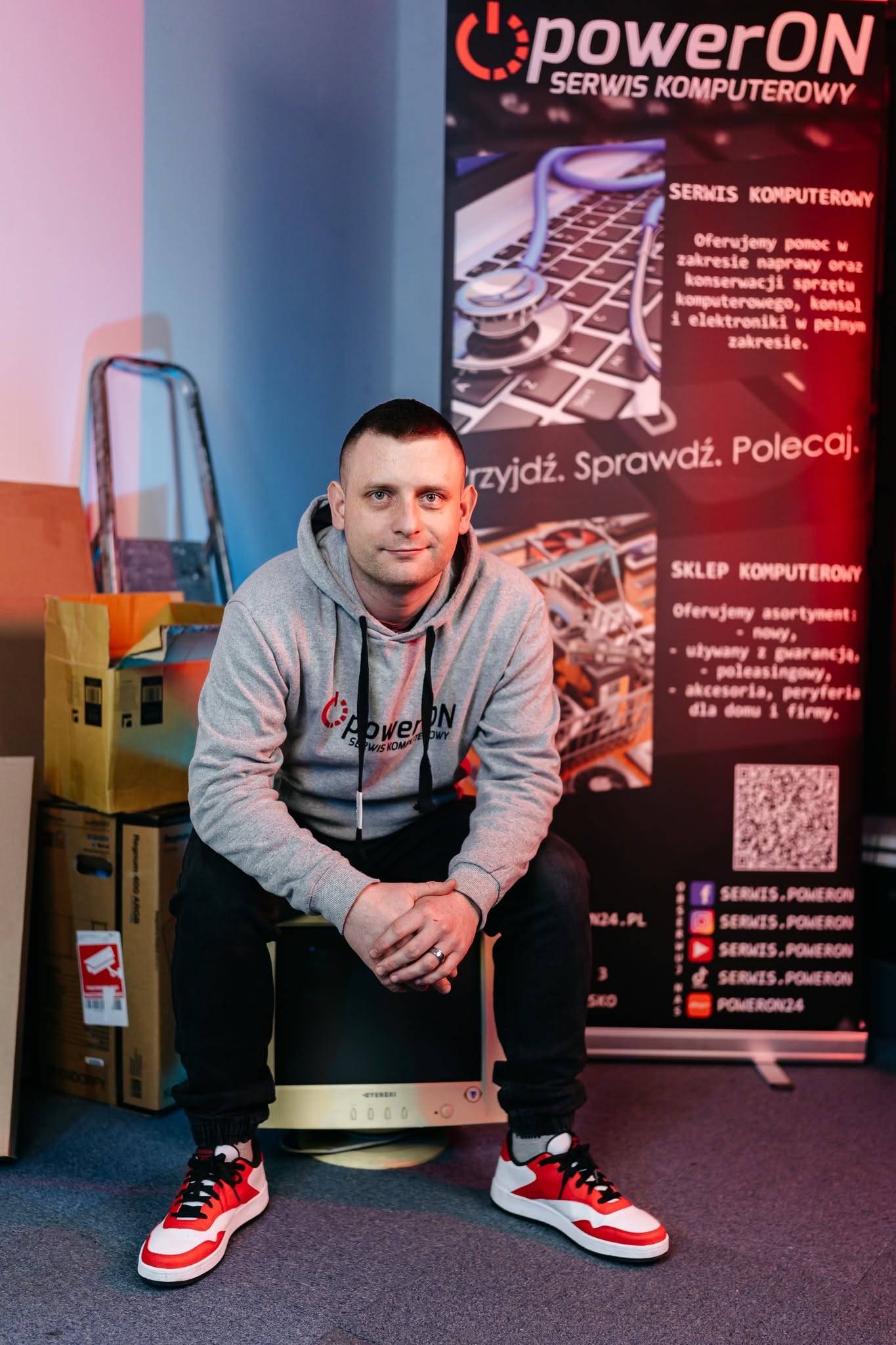 Mateusz Żebrowski, właściciel powerON – serwisu i sklepu komputerowego w Radomsku, na tle firmowego baneru.
