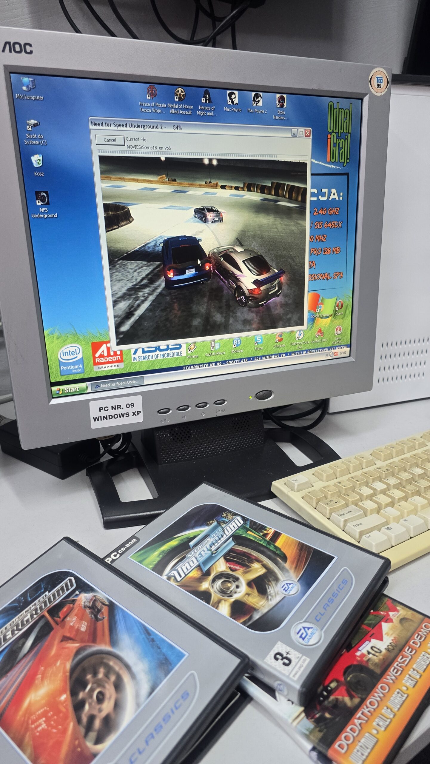 Monitor CRT AOC z uruchomioną grą wyścigową na Windows XP oraz pudełkowymi grami komputerowymi